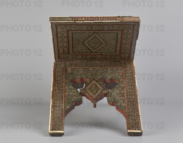 Quran lectern rahla, Islamic art, Persian art, Qajar dynasty 1785–1925, geometric ornament, stands, rahla, Quran, Persian culture, 19th century, Iran, piece of furniture; unfolded: length 21.5 cm, width 41.4 cm; folded: length 41.5 cm, width 16.5 cm, A decorative folding stand with an open top surface and carved legs, covered in intricate geometric and floral inlay patterns; the piece shows a central diamond motif on the top surface and matching diamond shapes on the inner area where the legs meet, with some carved scalloped edges and a small hanging element visible; the colors present include brown wood tones, dark and light beige or cream inlay, black detailing, and reddish-brown accents, set against a neutral gray background.