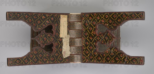 Quran lectern rahla, Islamic/Persian art, Qajar dynasty 1785–1925, geometric ornament, stand for Quran, Persian, 19th century, Iran, piece of furniture; unfolded: length 21.5 cm, width 41.4 cm; folded: length 41.5 cm, width 16.5 cm., An open ornate object with mirrored symmetrical halves connected by a central ribbed spine, each half covered in a dark background patterned with winding yellow vines and small red floral motifs, edged with thin red trim; the inner surfaces show darker inset panels with intricate geometric designs in muted browns and grays, and a few irregularly shaped cutouts revealing more patterned interior layers; a narrow vertical strip of light-colored worn material is attached near the spine with visible rough edges; the overall color palette includes black, yellow, red, brown, gray, and beige.