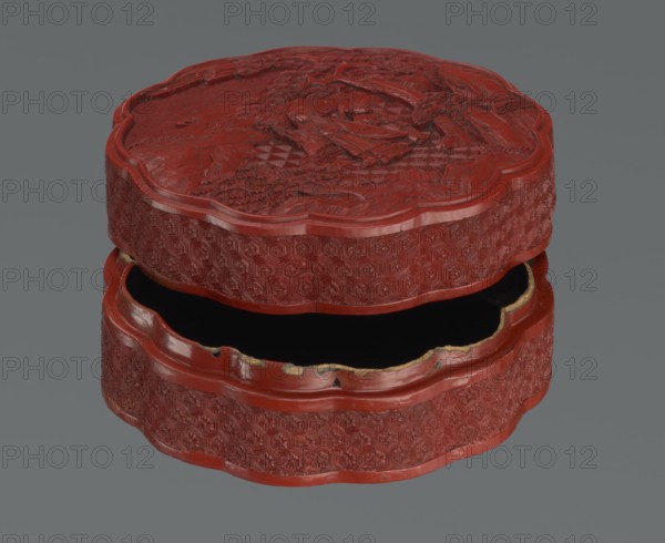 Box with a lid, Chinese, Qing dynasty 1644–1911, 2nd half of the 18th century. Lacquered box decorated with figurative scenes of sages and scholars with servants in landscape motifs featuring pine trees and rocks, rosettes, kikko tortoiseshell/hexagonal pattern and geometric ornament. Vessel; height 11.0 cm, width 4.8 cm., A round, carved box with a scalloped edge shown open, featuring a deep red color on its exterior and interior rim, a black interior visible inside, and a gray background; the box surface displays intricate raised geometric and floral carving on the sides and a carved scene with textured details on the lid, with some worn or chipped areas revealing a lighter, beige color along the inner edge.