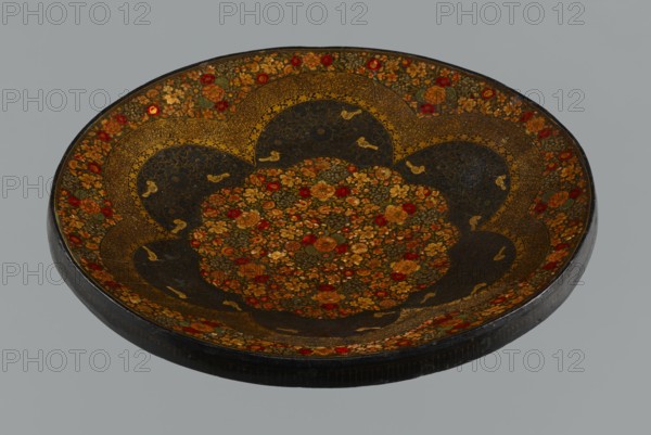 Plate, 19th century, Qajar dynasty 1785–1925, Persian, Iran; ceramic vessel, floral ornament with flowers; height 7.5 cm, diameter 42.0 cm., A shallow round tray with a scalloped central medallion filled with a dense floral pattern in shades of gold, red, orange, and green, set against dark, almost black background panels that alternate with intricately patterned gold bands; the rim and outer border repeat the floral motif with red and gold flowers and green leaves, and small gold bird-like shapes appear scattered within the dark panels; the tray edge is dark with subtle wear, and the overall visible colors include gold, red, orange, green, dark black, and hints of brown.