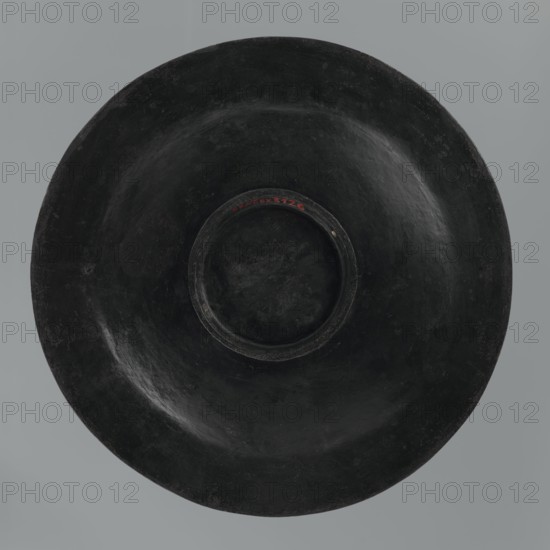 Plate, Islamic art, Persian culture, Qajar dynasty 1785–1925, floral ornament with flowers, 19th century, Iran, vessel, height 7.5 cm, diameter 42.0 cm, A large round object with a central recessed area, appearing smooth and worn, primarily black in color with slight variations in shade and subtle highlights; the background is a muted gray.