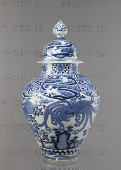 Vase with cover, Japanese, Edo 1603–1868, Genroku 1688–1704–Kyoho 1716–1736, ca. 1690–1730, Arita; porcelain, blue and white; decorated with phoenixes, hares/rabbits, peonies, chrysanthemums, lotuses; one of four elements of a fireplace set; vessel; height 59.0 cm, diameter 33.0 cm., A lidded ceramic vase with a bulbous body and a pointed finial lid decorated in blue on a white ground, showing ornate floral and curving motifs and stylized animal figures, with bands of patterned ornament around the neck and base; colors visible include blue, white, and gray, set against a neutral gray background.