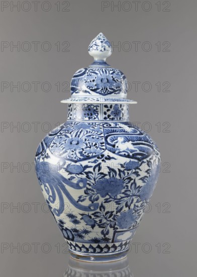 Vase with cover, unknown ceramist, Japanese, Edo period Genroku–Kyoho, ca. 1690–1730, Arita porcelain, blue-and-white decoration depicting phoenixes hoo, hares/rabbits, peonies, chrysanthemums, lotuses; one of a four-piece fireplace set; vessel, height 59.0 cm, diameter 33.0 cm., A blue and white porcelain lidded vase with a pointed finial, decorated all over with floral and foliate motifs and stylized birds, shown against a neutral gray background; visible colors include shades of blue, white, and gray.