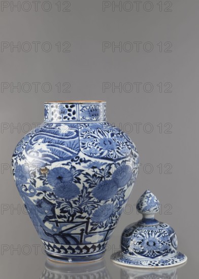 Vase with cover, unknown ceramist, Japanese, Edo period Genroku–Kyoho, ca. 1690–1730, Arita porcelain, blue-and-white decoration depicting phoenixes, hares/rabbits, peonies, chrysanthemums, and lotuses; one of the four elements of a fireplace set; vessel, height 59.0 cm, diameter 33.0 cm., A large blue-and-white porcelain jar with a rounded body and short neck sits beside a matching lid with a bulbous finial; both pieces feature dense floral and foliate designs in cobalt blue against a white ground, including stylized flowers, leaves, and decorative border panels, with the jar showing a band of geometric motif near its base and the lid echoing similar floral motifs and borders, all set against a neutral gray background with soft reflections beneath the objects.
