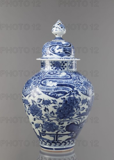 Vase with cover, unknown ceramist, Japanese, Edo period Genroku–Kyoho, ca. 1690–1730, Arita porcelain, blue-and-white, decorated with phoenixes, hares/rabbits, peonies, chrysanthemums, lotuses—kacho/kachoga flowers and birds iconography; one of four elements of a set; vessel height 58.0 cm, diameter 35.5 cm., A lidded ceramic jar with a bulbous body and pointed finial lid, decorated entirely with blue painted floral and decorative motifs on a white background, set against a neutral gray backdrop.