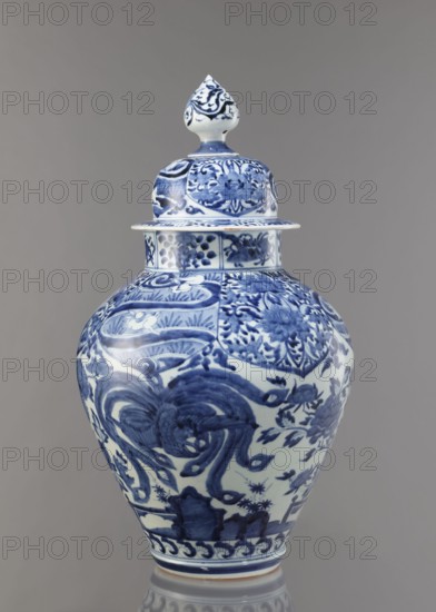 Vase with cover, Japanese, Edo period Genroku–Kyoho, ca. 1690–1730, Arita porcelain, blue-and-white decoration depicting phoenixes, hares/rabbits, peonies, chrysanthemums, lotuses — kachoga flowers and birds iconography; vessel height 58.0 cm, diameter 35.5 cm; one of four elements of a set; function: covered vase., A lidded ceramic jar with a bulbous body and a pointed finial lid, decorated in a blue and white palette; the surface shows intricate floral and scrolling motifs painted in various shades of blue on a white background, with decorative bands around the neck and base, and a glossy finish against a neutral gray backdrop.