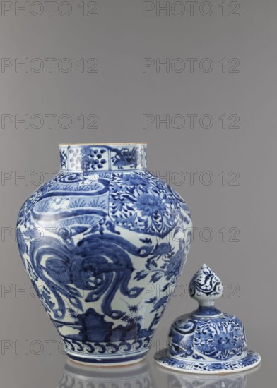Vase with cover, ceramist, Japanese, Edo period Genroku–Kyoho, ca. 1690–1730, Arita porcelain, blue-and-white porcelain; decorated with phoenixes, hares/rabbits, peonies, chrysanthemums, lotuses — kachoga flowers-and-birds iconography; one of four elements of a set; vessel height 58.0 cm, diameter 35.5 cm., A large ceramic vase and a matching lid positioned beside it, both decorated in blue on a white ground with intricate floral and abstract motifs; the vase has a rounded body with a short neck and detailed blue brushwork forming swirling shapes and floral panels, while the lid has a rounded finial and a domed base featuring similar floral patterns; the surface shows glossy reflections and a small area of exposed ceramic at the vase rim; the background is a smooth gray, and the visible colors are blue, white, gray, and a small hint of beige on the rim.