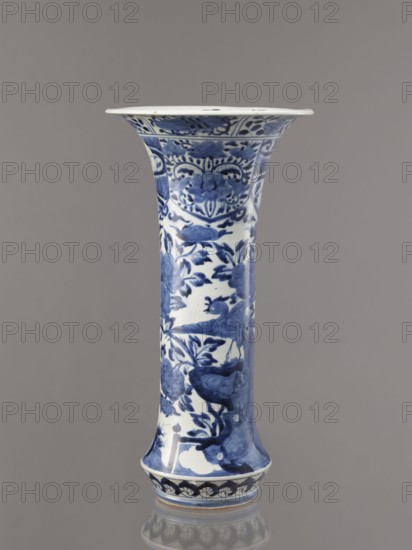 Vase, Japanese, Edo period Genroku–Kyoho, ca. 1690–1730, Arita; blue-and-white porcelain vessel, height 39.0 cm, dia. 20.3 cm; decorated with hares/rabbits, peonies, lotuses, phoenix hoo, kacho/flowers-and-birds iconography; one of four elements of a set., A tall porcelain vase shown against a plain gray background, predominantly white with blue painted decorative motifs; the vase has a flared rim and a slightly flared base, with a long narrow midsection covered in blue floral and bird designs, including stylized blossoms, leaves, and perched birds, along with ornate patterned bands near the rim and base, and a glossy finish that reflects light.