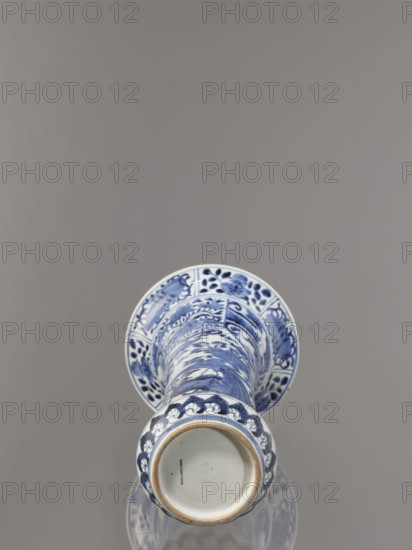 Vase, Japanese, Edo period 1603–1868, Genroku–Kyoho ca. 1690–1730, Arita, blue-and-white porcelain, decorated with hares/rabbits, peonies, lotuses, and phoenixes kacho/kachôga iconography, one of four elements of a set SKAZsz 314/1–4, vessel, height 39.0 cm, diameter 20.3 cm, A blue and white ceramic vase lying on its side against a smooth gray background, showing decorative blue floral and abstract patterns on white glaze, with a round open base and a rim that has a band of blue motifs, and a glossy surface that creates a subtle reflection on the surface beneath; visible colors include blue, white, gray, and a hint of beige on the unglazed edge.
