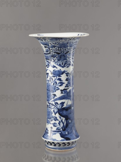 Vase, Japanese, Edo period Genroku–Kyoho, ca. 1690–1730, Arita; blue-and-white porcelain vessel, height 39.0 cm, diameter 20.3 cm; decorated with phoenixes hoo, hares/rabbits, peonies, chrysanthemums, lotuses — kacho/ kachoga flowers-and-birds iconography. One of four elements of a set; inscriptions/marks not specified., A tall, flared ceramic vase with a narrow waist and wide rim, decorated in blue on a white ground with intricate floral and bird motifs; the blue decoration includes stylized flowers, leaves, and a perched bird among branches, with decorative bands near the rim and base. The visible colors are blue, white, and subtle variations of gray on a neutral gray background.