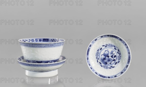 Bowl on a base with a lid, rice porcelain, Chinese, late 18th century Qing, 1644–1911. Ceramic vessel, height 10 cm. Geometric ornament, rice pattern and plant ornament, floral arrangement in a circle at the bottom. Signed., A group of porcelain bowls arranged against a light gray background, featuring white surfaces with blue decorative patterns; on the left a stacked pair with a smaller bowl nested inside a shallow dish, both showing blue floral and geometric bands along the rim and base, with glossy reflections on their surfaces, and on the right a single bowl displayed upright showing an inner circular floral motif in blue surrounded by a blue rim, all pieces resting on a reflective surface with subtle highlights and shadows.