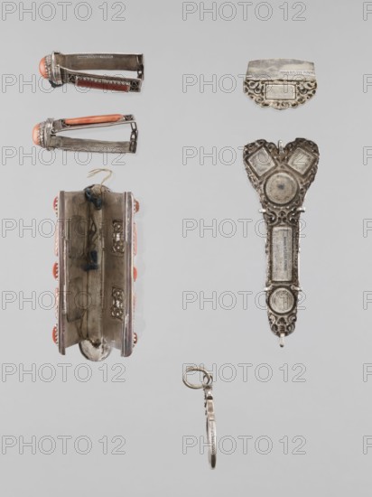 Braid ornament, braid ornament jewelry, artistic craft; women's ornament, 19th–20th century, Mongolia; height 3.0 cm, width 7.8 cm., A group of small metal objects arranged against a pale gray background includes a few elongated silver-toned clips with rounded coral-colored ends, a pair of open hinged metal casings showing interior compartments and small decorative cutouts, an ornate silver-toned pendant-like piece with filigree edges and circular raised areas, a small curved silver plate with decorative scalloped edge, and a thin dangling metal ring with a short attached bar; visible colors include silver, coral, and pale gray.