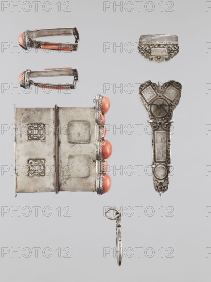 Braid ornament, braid ornament jewelry, Mongolian artistic craft, women's ornament, 19th–20th century, Mongolia; jewelry; height 3.0 cm, width 7.8 cm, The image shows a collection of small metallic objects arranged against a light gray background, including a folding rectangular piece with ornate cut-out panels and a hinge, a long decorative metal element with an intricate heart-shaped top and a circular motif, a separate scalloped metal plate, two similar cylindrical clip-like pieces set with rounded coral-colored stones, a vertical row of three round coral-colored cabochons set in metal bezels along one edge of the rectangular piece, and a small round metal hoop with an attached thin elongated metal tag; visible colors include silver-gray metal, coral orange stones, and the pale gray of the background.