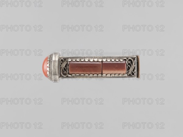 Braid clasp, braid ornaments, clasps, jewelry, Mongolian art, artistic crafts, women's ornaments, late 19th century, Mongolia, jewelry; height 2.9 cm, width 2.3 cm, length 7.4 cm, A small horizontal metallic object with decorative openwork on each end and a rectangular central section containing a group of reddish-brown cylindrical pieces; one rounded red-orange domed element is visible at the left end. The metal appears silvery with areas of darker patina, and the background is a pale gray.