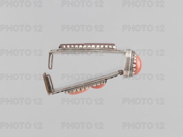 Braid clasp, braid ornaments, clasps, jewelry, Mongolian art, artistic crafts, women's ornaments, late 19th century, Mongolia, jewelry; height 2.9 cm, width 2.3 cm, length 7.4 cm, A metallic hinged object shown against a light gray background, photographed from the side, with a silver tone and slightly tarnished finish; the object has decorative scalloped metal edging and a few rounded coral-colored cabochon elements set into the metal; one coral element is prominent at the hinged end and a couple more are visible along the lower edge; the hinge and clasp components are visible with thin silver bars and a small looped hook; overall colors visible include silver, coral, and light gray.
