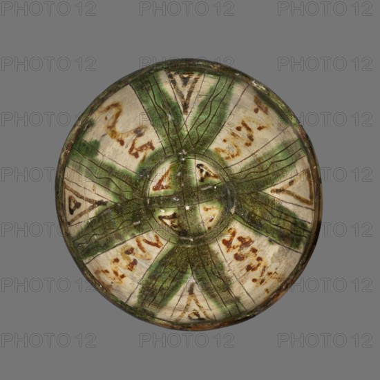 Bowl, Islamic art, Persian culture, glazed ceramic utility vessel with geometric motifs, 12th–13th century, Afghanistan; weight 0.376 kg, height 8.8 cm, diameter 17.5 cm, A round ceramic bowl viewed from above with a central circular depression and a radiating pattern; the surface shows a banded design with a group of green brushstrokes forming a star-like cross radiating from the center, alternating with off-white segments that have scattered brownish marks; the glaze has a crackled texture and areas of darker green and brown along the rim; the overall colors visible are green, off-white, brown, darker brown, and touches of black against a neutral gray background.