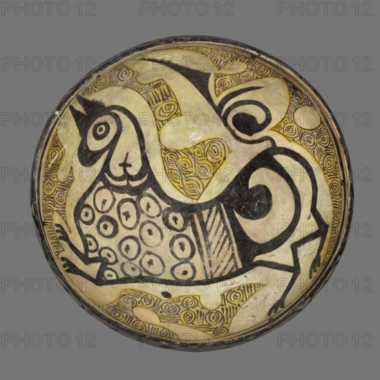 Bowl, Islamic art, Persian culture, ceramics, griffins, Persian ceramics, 10th century, Iran, vessel, weight 1.47 kg, height 13.5 cm, diameter 30 cm, A round shallow bowl with a painted interior showing a stylized bird-like creature with rounded body, curved neck, and a pointed head, rendered in black outline and filled areas on a pale yellowish background; the creature's body is decorated with a pattern of several circular motifs and a section of diagonal stripes, and its tail and legs are depicted with bold black curved lines; the surrounding interior surface contains areas of intricate repeating spiral motifs and irregular pale yellow shapes, all enclosed by a thin dark rim; visible colors include pale yellow, black, cream, and touches of muted brown.