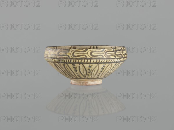 Bowl, Islamic art, Persian culture, ceramics, Persian ceramics, images of birds, birds, palmettes ornament, 10th century, Nishapur, Iran; vessel; weight 1.11 kg; height 12.1 cm; diameter 26.0 cm, A shallow ceramic bowl with a rounded profile and small foot sits centered on a smooth reflective surface, showing a faint reflection beneath it. The bowl features painted decorative bands and motifs in shades of cream, beige, black, and brown; the upper rim has a repeating curved pattern in darker tones on a lighter background, a narrow band of short vertical strokes encircles below it, and the lower portion displays elongated leaf-like shapes and small dash marks arranged around the exterior. The interior rim shows a continuation of darker paint, and the foot has a slightly reddish-beige hue. The background is a uniform muted gray.
