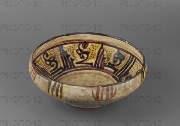 Bowl, Islamic art, Persian culture, inscriptions, calligraphy, Persian pottery, ceramics, 9th–10th century, Iran, vessel, weight 0.76 kg, height 9.9 cm, diameter 25 cm, A shallow round bowl photographed against a gray background, showing an interior decorated with abstract dark brown and black linear and curvilinear patterns on a yellowish ground and a pale beige base; the rim and outer surface show bands and vertical stripe motifs in brown and reddish-brown on a mottled beige exterior, with areas of wear and small chips visible.
