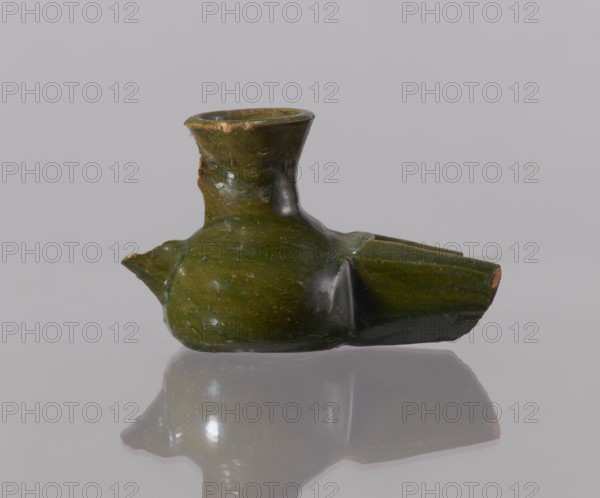 Oil lamp, Islamic art, Arabic culture, 12th century Egypt; Arabic pottery utility oil lamp used in everyday life in the Middle East; height 6.0 cm, width 10.4 cm, depth 5.5 cm, A small green ceramic vessel with a glossy finish sits on a reflective surface against a pale gray background, showing a rounded body, a short narrow neck with a flared rim, and a broken spout-like extension; the glaze is mostly olive to dark green with areas of lighter green and small patches of exposed reddish-brown clay at damaged edges, and the reflection of the vessel appears below it on the surface.