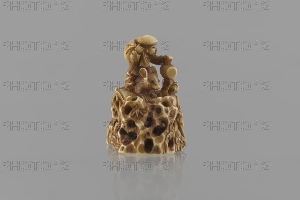 Netsuke in the shape of Daikoku and Ebisu, Ryôji fl. ca. 1886–1900? sculptor, Japanese, Meiji 1868–1912, figurines, netsuke, Daikoku deity, Ebisu deity, carps, rats, sea waves, mythology. From the group of seven gods of all happiness come two figures, finely carved in a miniature rocky landscape with a bridge: Daikoku, sitting on a rat and holding his inherent attribute—a hammer—in his left hand and a bag on his back; and Ebisu holding a fishing rod and riding a giant fish. The miniature is 3.9–4.0 cm high/wide, carved with meticulous details: facial features, scales on the fish, bamboo leaves on openwork rocks, the rat's fur, and the rodent's eyes marked with microscopic inlays of black-dyed bone. 4th quarter of the 19th century, Japan., A small carved object in shades of beige, tan, and brown sits centered against a smooth gray background, showing a glossy surface and a soft reflection beneath it; the carving depicts a group of organic shapes with textured holes and contours, a detai...