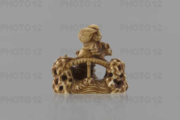 Netsuke in the shape of Daikoku and Ebisu, Ryôji fl. ca. 1886–1900? sculptor, Japanese, Meiji 1868–1912, figurine netsuke katabori, Daikoku deity, Ebisu deity, carps, rats, sea waves, mythology. Two figures from the seven gods of all happiness carved in a miniature rocky landscape with a bridge: Daikoku seated on a rat holding a hammer in his left hand and a bag on his back, and Ebisu holding a fishing rod and riding a giant fish. The miniature is 3.9–4.0 cm height 3.9 cm, width 4.0 cm. Finely carved details include facial features, fish scale outlines, bamboo leaves on openwork rocks, the rat’s fur, and the rodent’s eyes with microscopic black-dyed bone inlays. 4th quarter of the 19th century, Japan., A small carved object sits on a reflective surface against a plain gray background, showing a figure wearing a head covering riding on the back of an animal perched atop a textured base with organic, porous-looking forms; the carving displays a range of beige, tan, brown, and cream tones...