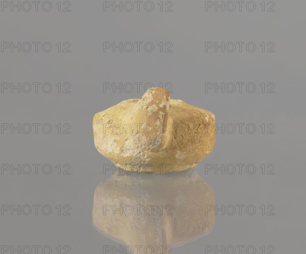 Oil lamp, Islamic Arabic culture, utility ceramics, Arabic/Egyptian ceramics, everyday life in the Middle East, 8th–9th century, Egypt; oil lamp; height 9.4 cm, width 5.7 cm, depth 4.1 cm, A rough, irregularly shaped object with a protruding knob sits centered against a smooth background, showing colors of yellow, ochre, beige, and patches of pale white and light brown; the object has a textured, mottled surface and is reflected below on a glossy surface that mirrors its form and colors.