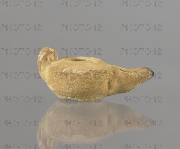 Oil lamp, Islamic art, Islamic and Arabic culture, utility ceramics, Arabic ceramics, everyday life in the Middle East, Egyptian ceramics, 8th–9th century, Egypt place of origin, oil lamp, height 9.4 cm, width 5.7 cm, depth 4.1 cm, A weathered oil lamp shaped like a shallow bowl with a pronounced spout and a rounded handle, shown on a reflective surface that creates a soft mirror image; the lamp has a rough, uneven texture with patches of lighter wear and small areas of greenish discoloration, and the visible colors include shades of tan, ochre, brown, pale yellow, and hints of green against a neutral gray background.