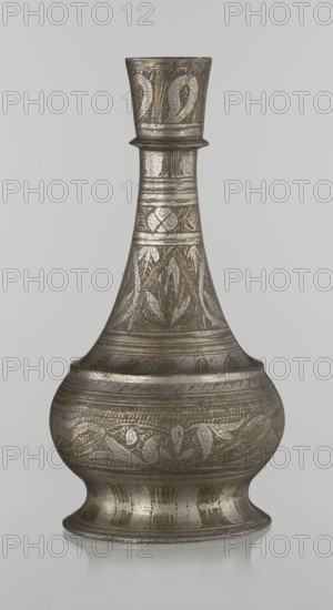 Bottle, Islamic art, Arabic, early 20th century, Middle East. Vessel with neck slender towards the top, ending with a straight spout; engraved geometric and plant motifs painted with golden-brown paint. Height 21.6 cm; width 10.5 cm., A metallic vessel with a narrow neck flaring into a wider base, shown against a plain light gray background; the vessel has an overall aged silver-gray and muted gold patina with darker gray and brownish areas, and is decorated with engraved repeating leaf and geometric patterns covering the neck and body; a small rounded collar separates the upper neck from the wider midsection, and the base is slightly flared with bands of engraved ornamentation; the surface shows fine textured markings and areas of wear that create subtle variations in silver-gray, gold, brown, and dark gray tones.