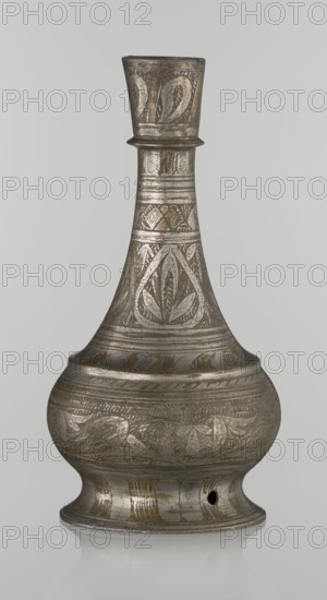 Bottle, Islamic art, Arabic culture, geometric ornament, plant motifs. Neck slender towards the top, ending with a straight spout. Engraved patterns painted with golden-brown paint. Early 20th century, Middle East. Vessel. Height 21.6 cm, width 10.5 cm., A metal vessel with a narrow flared neck rising from a rounded body, featuring engraved decorative bands and stylized leaf and floral motifs; the surface shows a mix of metallic gray and darker patinated brown tones with lighter silver highlights; a small circular hole near the base; the vessel sits on a flared foot and displays a worn, slightly reflective finish.