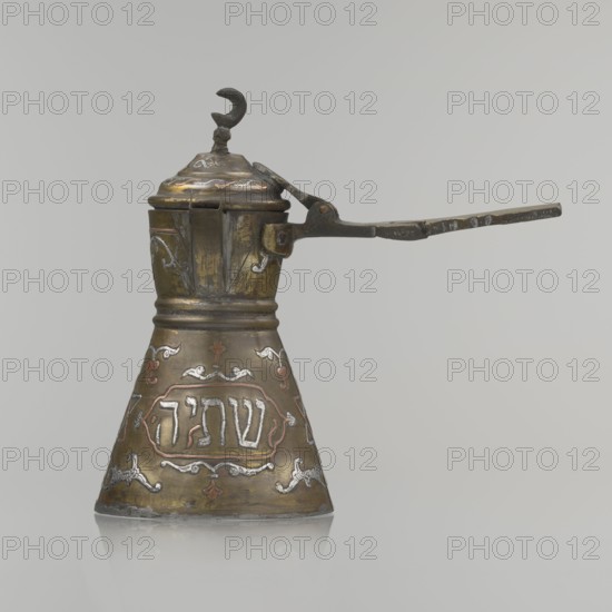 Coffee pot, Arabic and Jewish cultural influences, beverages coffee, cezve vessel; Decoration: Hebrew inscriptions inlaid in copper, Star of Solomon motif, arabesque patterns; hinged lid with hinge halfway down the handle, lid topped with a crescent. Inscriptions deciphered: reads drinking; in the hexagonal star Gan Eden, garden; in the cartouche for celebration; under the handle, in the Seal of Solomon/Star of David the letter Mim from the word water. Beginning of the 20th century, Palestine; vessel; height 15.5 cm, width 15.5 cm, diameter 8.7 cm., An ornate metal vessel with a conical base and a narrower upper neck, finished in aged brass tones with areas of darker patina and hints of silver and copper inlaid decoration, a hinged domed lid topped by a small crescent-shaped finial, a long flat iron handle attached to the upper section, and decorative scrolling motifs around the body in silver and copper tones against the brass surface.