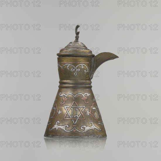 Coffee pot, gift; Arabic and Jewish cultural influences; beverages, coffee; cezve vessel; inscriptions; crescent symbol; six-pointed star iconographic. Decoration: Hebrew inscriptions inlaid in copper, Star of Solomon motif, and arabesque patterns. Hinged lid, hinge halfway down the handle; lid topped with a crescent. Inscriptions deciphered: drinking; in the hexagonal star Gan Eden, garden; in the cartouche for celebration; under the handle, in the Seal of Solomon/Star of David Mim from the word water. Beginning of the 20th century, Palestine; vessel; height 15.5 cm, width 15.5 cm, diameter 8.7 cm., A metal pitcher with a conical base and a narrower neck and lid, showing a patinated surface in brassy gold and bronze tones with areas of darker brown; decorative raised scrollwork and motifs in silvery white and coppery pink wrap around the body and neck; a curved spout extends from the upper side and a small ornate finial tops the lid, all set against a pale gray background.