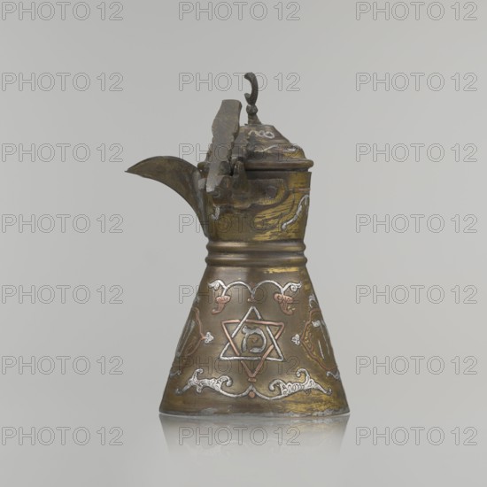 Coffee pot, gift; Arabic and Jewish cultural influences; beverages, coffee; cezve vessel; Decoration: Hebrew inscriptions inlaid in copper, Star of Solomon motif, and arabesque patterns; hinged lid with hinge halfway down the handle; lid topped with a crescent. Inscriptions deciphered: drinking; in the hexagonal star Gan Eden, garden; in the cartouche for celebration; under the handle, in the Seal of Solomon/Star of David Mim from the word water. Early 20th century, Palestine; vessel; height 15.5 cm, width 15.5 cm, diameter 8.7 cm., An ornate metal pitcher with a hinged lid and curved spout sits against a neutral gray background; the pitcher is conical in shape and displays a mix of metallic colors including brassy gold, dark bronze, silver, and hints of copper, with decorative engraved and inlaid motifs around its body, a curved handle attached to the lid, and a reflective surface at the base creating a subtle mirror effect.