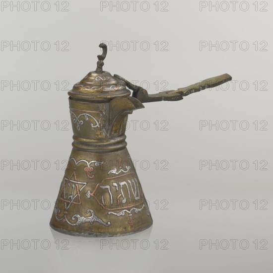 Coffee pot, beginning of the 20th century, Palestine. Cezve vessel for coffee, height 15.5 cm, width 15.5 cm, diameter 8.7 cm. Materials: copper with inlaid decoration. Decoration: Hebrew inscriptions inlaid in copper, Star of Solomon motif six-pointed star, arabesque patterns, crescent symbol; hinged lid with hinge halfway down the handle and lid topped with a crescent. Inscriptions deciphered: words including drinking; in the hexagonal star Gan Eden, garden; in a cartouche for celebration; under the handle, in the Seal of Solomon / Star of David Mim from the word water. Cultures: Arabic, Jewish., A metal vessel with a hinged lid and a long handle is shown against a plain light gray background. The vessel has a conical base that tapers up to a narrower neck and rounded shoulder, and a curved spout extends from the upper body. The hinged lid has a small decorative finial and the handle connects to the lid mechanism with a pivot. The surface of the object shows metallic tones of brass, ...