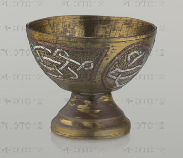 Bowl, early 20th century, Palestine, Middle East. Vessel, height 4.7 cm, diameter 5.5 cm. Islamic art; Arabic inscriptions and calligraphy; decoration with braid and stylized Arabic inscriptions in cartouches; punched background; geometric motifs., The image shows a metal goblet with a rounded bowl on a flared stem and base, featuring decorative raised patterns around the bowl. The surface displays worn metallic tones including gold, brass, copper, and silver, with areas of darker brown patina and patches where the finish is rubbed. The decorative panels have textured dot backgrounds and braided raised motifs in a silvery color outlined with a reddish-copper accent, and the interior of the bowl shows a scratched golden surface. The base reflects the same gold and brown wear, and the object sits on a neutral pale gray background.