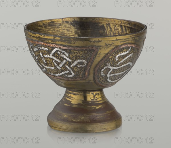 Bowl;, Decoration with braid and stylized Arabic inscriptions in cartouches; punctured background; Arabic inscriptions and calligraphy; geometric motifs; vessel; early 20th century; Palestine possible origin; height 4.7 cm, diameter 5.5 cm., A small metal bowl on a short pedestal is shown against a light gray background, with a worn golden surface and areas of darker brown and black patina; the bowl's exterior features a few raised decorative panels with interlacing patterns in metallic silver and copper tones set against a textured dark area, and the interior shows scraped gold and dark streaks.