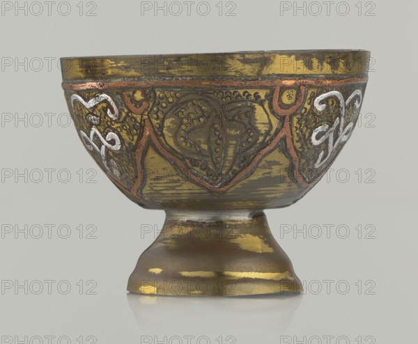 Bowl, 20th century, Middle East possibly Palestine. Ceramic vessel with arabesque and geometric motifs and punched background; height 4.3 cm, diameter 5.6 cm. Islamic art, Arabic., A metal goblet with a rounded bowl and flared foot sits against a plain light gray background; the surface of the goblet shows worn metallic finishes in gold, brass, and brown with areas of darker tarnish and lighter reflective patches, and decorative raised patterns in reddish-brown and silvery-white that form curving and organic shapes around the bowl, along with textured dotted details and scalloped borders.