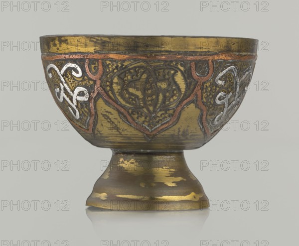 Bowl, ; Islamic art, Arabic; arabesque ornament, geometric motifs, punched background; 20th century; Middle East, possibly Palestine; vessel; height 4.3 cm, diameter 5.6 cm., A metal bowl with a flared foot, shown against a neutral light gray background, featuring a worn metallic surface in gold tones with patches of darker brown and muted black wear; the bowl's exterior is decorated with raised ornamental patterns outlined in a copper-colored metal and filled with textured dark areas, and several curving decorative motifs in a silvery white accent are visible on the sides; the rim shows darker patina and the foot has irregular gold and brown patches with small areas of brighter yellowish gold.