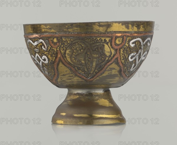 Bowl, 20th century, Palestine, Middle East; Islamic art, Arabic; vessel with arabesque and geometric motifs, punched background; height 4.3 cm, diameter 5.6 cm., A shallow metal bowl on a flared pedestal base, showing an aged metallic surface with gold, brass, brown, copper, and silver tones; the bowl exterior has decorative raised patterns with curved and looping motifs in copper and silver against a darker gold-brass ground, and areas of worn finish and patina revealing brown and darker metallic patches; the pedestal has irregular gold highlights and darker brown areas, and the whole object sits on a reflective neutral surface with a pale gray background.