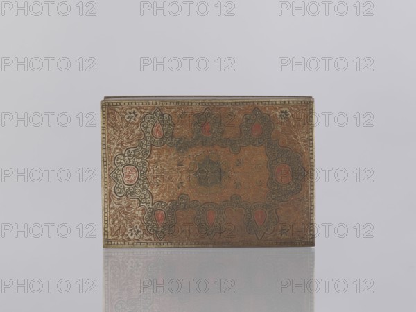 Box with lid. Indian, North India, 1st half of the 20th century. Box decorated on the sides with plant twigs; paste colors: red, orange, black paste pressed into engraved patterns. Materials/genre: applied art; smoking accessories/casket/box. Dimensions: height 2.8 cm, width 12.8 cm, depth 9.0 cm., A rectangular ornate box with an intricate patterned top sits centered on a light gray background, showing detailed floral and paisley-like decorations in muted gold, brown, red, and dark gray tones with hints of black; the box has a thin decorative border and a subtle reflection beneath it on the glossy surface.