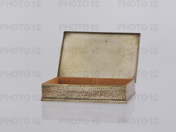 Box with lid. Indian, North India, 1st half of the 20th century. Applied art; smoking accessory/casket/box. Decorated on the sides with plant twigs; geometric ornaments. Paste colors: red, orange, black paste pressed into engraved patterns. Height 2.8 cm; width 12.8 cm; depth 9.0 cm., An open rectangular box with a hinged lid sits on a reflective surface; the box exterior shows ornate patterned decoration in metallic gold and brown tones, the interior base is a warm reddish-brown, and the inside of the lid is a pale, aged off-white with subtle mottling; the background is a smooth, light gray.