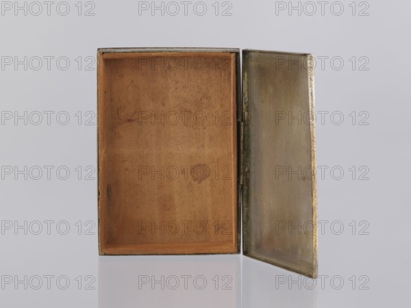 Box with lid., Indian, North India. Early 20th century 1st half of the 20th century. Smoking accessory/casket/box in applied art. Box decorated on the sides with plant twigs; geometric ornaments. Paste colors: red, orange, black paste pressed into engraved patterns. Height 2.8 cm, width 12.8 cm, depth 9.0 cm., An open rectangular box with its lid swung outward showing the interior lined in a warm brown material with visible wear marks and a few darker spots, and the lid interior appearing metallic with a muted gold and brass tone; the exterior edges of the box show darker brown and black trim, and the background is a soft light gray with a reflective surface beneath the box mirroring the bottom edge.