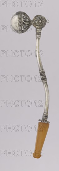 Pipe for smoking hashish, Islamic art, Arabic culture; stimulants, narcotics, smoking accessory. The stem is slightly curved, thin, ending with a flattened amber, mouthpiece. A short silver pipe used for smoking hashish — a hallucinogenic drug produced from cannabis flowers. A lump of compressed substance was placed in the recess at the end of the pipe. The mouthpiece is amber, and the main part is decorated using the filigree technique — ornaments formed from thin wires joined into intricate patterns. 1st half of the 20th century, Yemen; pipe; height 12.5 cm, width 1.7 cm., A curved metallic object with decorative filigree and floral motifs attached to a spherical cage-like element at one end, and a tapered amber-colored handle at the other; visible colors include silver tones on the metal and warm amber on the handle, set against a light gray background.