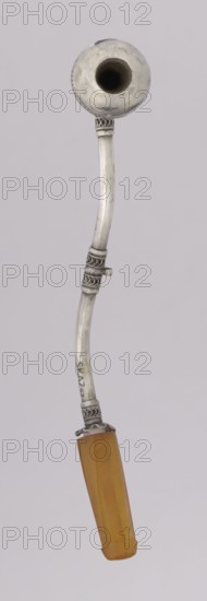 Pipe for smoking hashish. The stem is slightly curved, thin, ending with a flattened amber, mouthpiece. The short silver pipe may have been used for smoking hashish — a hallucinogenic drug produced from cannabis flowers. A lump of the compressed substance was placed in the recess at the end of the pipe. The mouthpiece was made of amber, and the main part of the object was decorated using the filigree technique — creating ornaments from thin wires joined into intricate patterns. 1st half of the 20th century, Yemen. Pipe; height 12.5 cm, width 1.7 cm., A long curved object with a rounded hollow bowl at the top and a faceted handle at the bottom, rendered in metallic silver and warm amber tones; the silver shaft has a few decorative banded sections with looped filigree and a small protruding tab, showing slight surface wear and subtle scratches, while the amber handle is translucent with vertical facets and a smooth glossy finish; the background is a uniform pale gray.