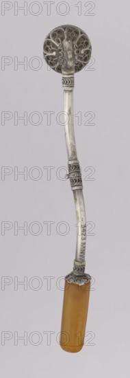 Pipe for smoking hashish, Islamic art, Arabic, stimulants, narcotics, smoking accessory. The stem is slightly curved and thin, ending with a flattened amber, mouthpiece. The short silver pipe may have been used for smoking hashish; a lump of compressed substance was placed in the recess at the end. The mouthpiece is amber, and the main part is decorated with filigree—ornaments made from thin wires joined into intricate patterns. 1st half of the 20th century, Yemen; pipe; height 12.5 cm, width 1.7 cm., A vertical object with a round ornate top in a silver-gray metal showing filigree and curved decorative elements, a long slightly curved silver-gray shaft with textured decorative bands and a small protruding peg, and a cylindrical handle in a translucent amber-orange color capped with a silver-gray ornate collar; the background is a uniform light gray.
