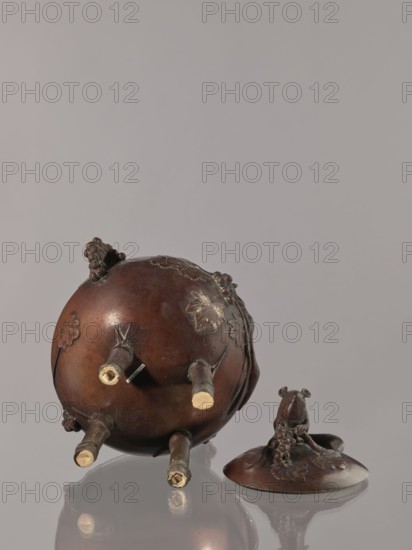 Censer kôro, Japanese, Meiji period 2nd half of the 19th century. Vessel, height 26.0 cm, width 22.5 cm, weight 2.84 kg. The cover is topped with a full-plastic figurine of a squirrel. The belly is decorated in high relief with a motif of a squirrel on a vine. Two handles are in the shape of grape clusters. Japanese art; motifs: squirrels, grapes., A round, brown metal vessel lies on its side with a few short cylindrical protrusions extending outward and several raised leaf and grape cluster decorations on its surface, next to a separate brown metal lid topped by a small sculpted animal figure perched among a cluster of grapes and leaves; the background is a uniform pale gray and the objects cast soft reflections on the glossy surface beneath them, with visible colors including brown, pale beige at the ends of the protrusions, and gray.