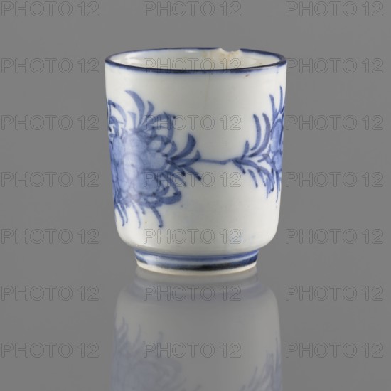 Bowl, gift, Chinese, Qing 1644–1911, 19th/20th century. Ceramic vessel on a ring-shaped foot, height 5.5 cm, diameter 4.7 cm. Decorated with stylized floral sprigs and tendrils. Signature in the bottom ring., A small cylindrical ceramic cup sits upright on a reflective surface, showing a white base color with blue decorative floral motifs and blue rim accents; the visible colors are white, blue, gray, and a few subtle beige spots, with the cup casting a soft reflected image and a neutral gray background.