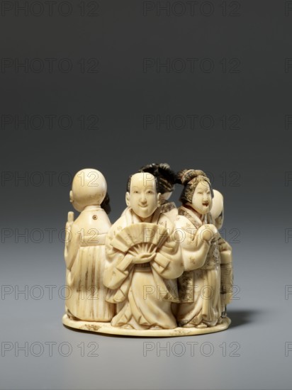 Okimono in the shape of a group of six singing people; material: sculpture; style/culture: Japanese, Meiji period late 19th century; subject: six figures— a courtesan with a small kamuro servant, a townswoman carrying a lantern, a wealthy merchant with a fan, a messenger holding an oblong box, and a blind Buddhist monk with a shaved head leaning on a cane; type: figurines/okimono; maker:, dimensions: height 5.1 cm, width 5.2 cm, depth 4.5 cm., A small carved ivory group showing a few figures arranged in a circle on a rounded base, each figure wearing flowing garments with carved folds and patterned details; the front figure holds a folding fan and has a smooth, pale ivory face with dark carved hair, while another figure beside them has a similarly pale face and an elaborate coiffure with darker hair tones and holds a cylindrical object; additional figures around the back show shaven and smooth heads and robes with vertical carved lines; the object rests on a neutral gray surface agains...