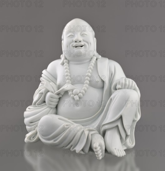 Budai Laughing Buddha, 19th century, China, Fujian; Qing dynasty; Chinese art; Budai iconography — Buddha of the Future, Maitreya Milefo; figurine; height 30.4 cm, width 21.6 cm, weight 3 kg., A glossy white ceramic statue of a seated smiling figure wearing draped robes and a beaded necklace, shown against a smooth gray background; the figure has a rounded belly, relaxed crossed legs, one hand resting on a knee and the other holding a small object, with detailed folds in the fabric and a reflective surface that creates subtle highlights and shadows in white and gray.
