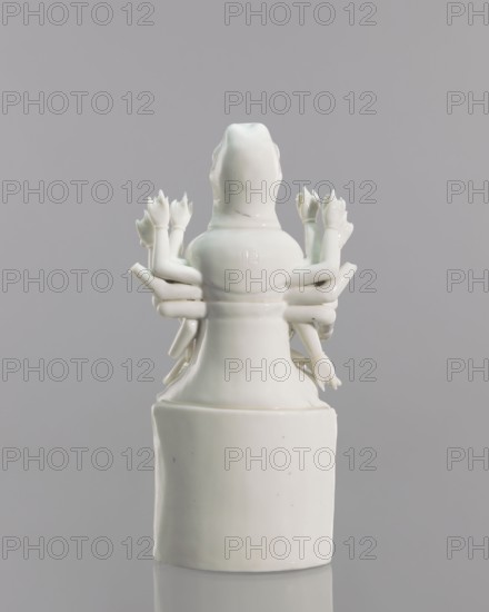 Guanyin on a lotus throne, Chinese, Blanc de Chine porcelain sculpture, 18th century, Fujian, China; subject: Guanyin goddess from Chinese Buddhism; height 27.0 cm, width 14.3 cm; inscriptions/provenance: repossession Jelenia Góra noted., A glossy white ceramic figurine shown from the back against a neutral gray background, featuring a rounded head and a tapered torso mounted on a cylindrical base, with a group of several small sculpted arms extending outward from the sides, each arm ending in a stylized hand or flower-like form; the surface shows subtle reflections and a few tiny dark specks.